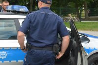 Obraz przedstawia dzielnicowego o na tle radiowozu policyjnego na imprezie plenerowej w Czyżewie