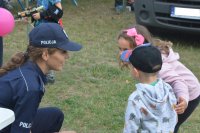 Obraz przedstawia policjantkę  rozmawiająca z dziećmi  na imprezie plenerowej w Czyżewie
