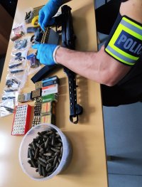 Obraz przedstawia zabezpieczoną amunicję, pistolet i rewolwer oraz dłonie policjanta zabezpieczającego przedmioty