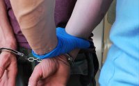 Obraz przedstawia dłonie policjanta trzymającego dłonie zatrzymanego w kajdankach