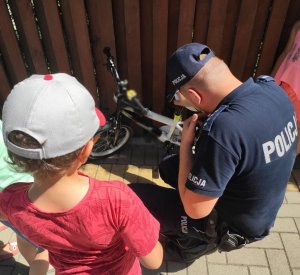 Obraz przedstawia policjanta znakującego rower