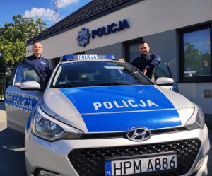 Obraz przedstawia policjantów dzielnicowych z Sokół na tle radiowozu