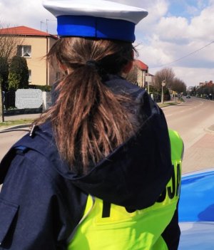 Obraz przedstawia policjantkę wydziału ruchu drogowego stojącą tyłem na jednej z ulic w Wysokiem Mazowieckiem
