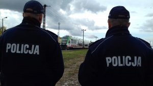 Obraz przedstawia policjantów dzielnicowych w miejscowości Sokoły. W tle widać przejeżdżający pociąc