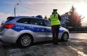 Obraz przedstawia radiowóz policji na jednej z ulic w Wysokiem Mazowieckiem. W tle widać policjantkę
