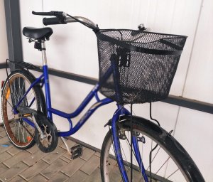Obraz przedstawia rower koloru niebieskiego z koszykiem