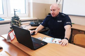 Obraz przedstawia aspiranta Grzegorza Kruszewskiego siedzącego przed laptopem