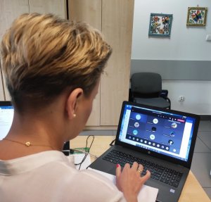 Obraz przedstawia profilaktyk siedzącą przed laptopem prowadzącą zajęcia online