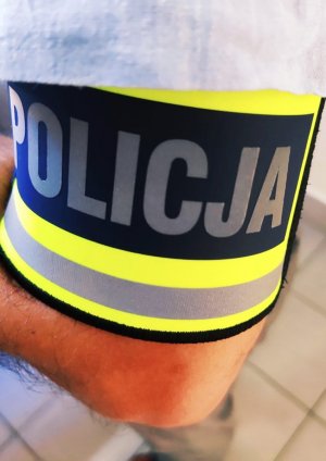 obraz przedstawia ramię mężczyzny z założoną opaską, na której widnieje napis policja