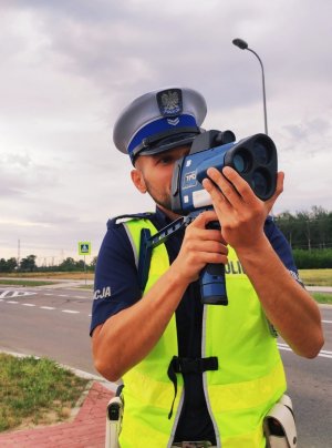 obraz przedstawia policjanta trzymającego w ręce urządzenie do pomiaru prędkości