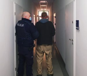 obraz przedstawia policjanta z mężczyzną na korytarzach budynku Policji
