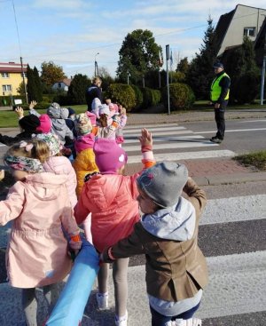 obraz przedstawia policjant patrzącego na grupę dzieci przechodzących przez przejście dla pieszych