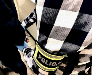 obraz przedstawia policjanta z opaską na ramieniu z napisem  policja zakładającego kajdanki na ręce