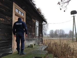 obraz przedstawia policjanta na tle drewnianego budynku