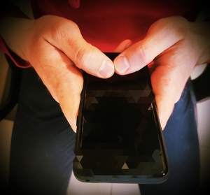 obraz przedstawia dłonie trzymające telefon komórkowy