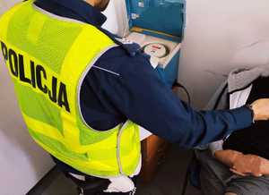 obraz przedstawia policjanta obsługującego urządzenie do badania stanu trzeźwości