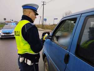 obraz przedstawia policjanta stojącego przy samochodzie