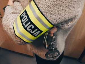 obraz przedstawia ramię policjanta z opaską odblaskową z napisem policja