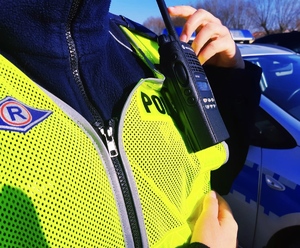 obraz przedstawia kamizelkę odblaskową policjanta oraz urządzenie do utrzymywania łączności