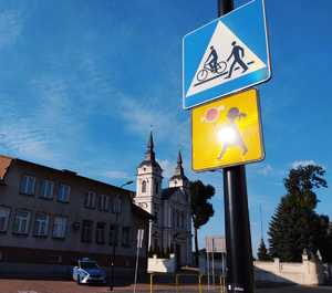 obraz przedstawia radiowóz, w tle budynek kościoła i znaki drogowe