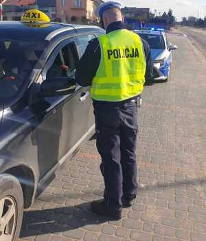 obraz przedstawia policjanta kontrolującego taksówkarza
