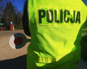 obraz przedstawia policjanta w kamizelce odblaskowej z napisem policja, w ręku trzyma tarczę do zatrzymywania pojazdów