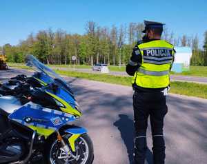 obraz przedstawia policjanta  stojącego przy motocyklu