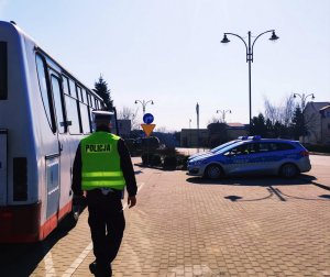 obraz przedstawia policjanta idącego przy autokarze, w tle radiowóz