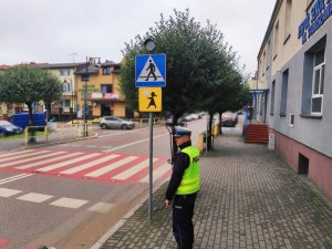 obraz przedstawia policjanta sprawdzającego oznakowanie przy szkole w Wysokiem Mazowieckim, w tle pojazdy i budynek szkoły