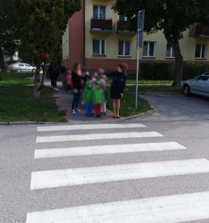obraz przedstawia policjantkę przeprowadzającą dzieci przez przejście dla pieszych