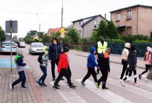 obraz przedstawia policjanta przeprowadzającego dzieci przez przejście dla pieszych