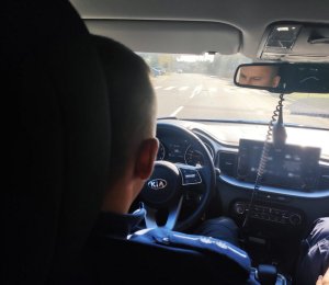 obraz przedstawia policjanta siedzącego za kierownicą pojazdu