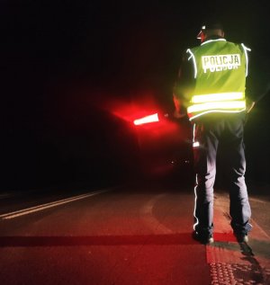 obraz przedstawia policjanta trzymającego urządzenie do zatrzymywania pojazdów nocą
