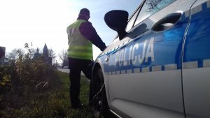 obraz przedstawia policjanta stojącego przy radiowozie