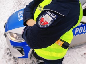 obraz przedstawia ramię policjanta z naszywką, na której widnieje napis Wydział Ruchu Drogowego, w tle radiowozu