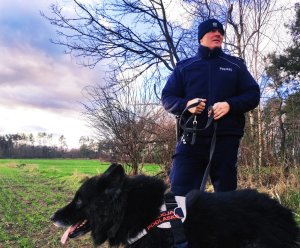 obraz przedstawia policjanta z psem na tle masywu leśnego