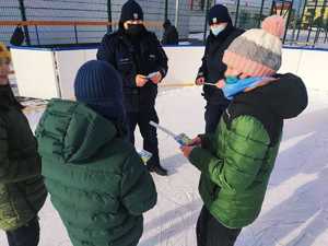 obraz przedstawia policjantów rozmawiających z dziećmi na lodowisku