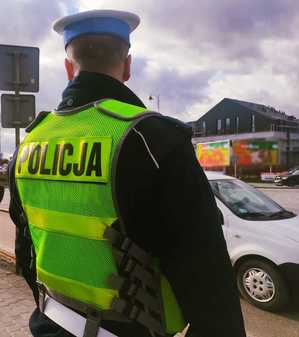 obraz przedstawia stojącego policjanta przed przejściem dla pieszych, w tle pojazdy
