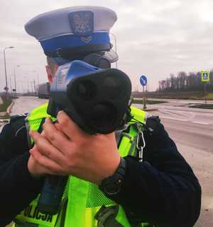 obraz przedstawia policjanta trzymającego w ręce urządzenie do pomiaru prędkości