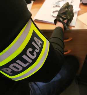 obraz przedstawia ramię mężczyzny z opaską na ramieniu z napisem policja