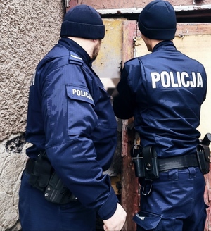 obraz przedstawia umundurowanych policjantów na tle drewnianego budynku