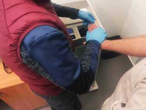 obraz przedstawia dłonie mężczyzny w rękawiczkach wykonujące czynności na urządzeniu do daktyloskopii