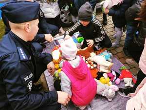 obraz przedstawia policjantów na spotkaniu z dziećmi, dzieci wybierają pluszaki