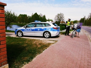 obraz przedstawia policjanta rozmawiającego z rowerzystką, w tle radiowóz