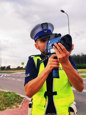 obraz przedstawia policjanta trzymającego urządzenie do pomiaru prędkości