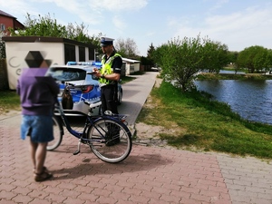 obraz przedstawia policjanta rozmawiającego z rowerzystką, w tle radiowóz