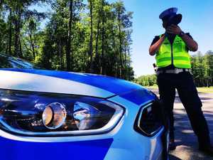 obraz przedstawia policjanta trzymającego urządzenie do pomiaru prędkości, w tle radiowóz oraz masyw leśny