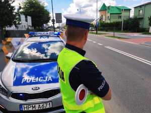 obraz przedstawia policjanta obserwującego przejście dla pieszych, w tle radiowóz