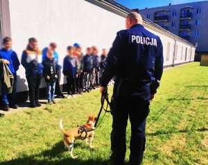 obraz przedstawia policjantów na spotkaniu z grupą dzieci, policjanci pokazują psa służbowego