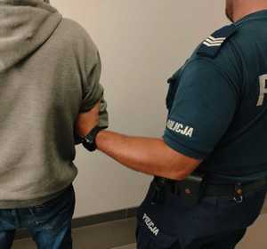 obraz przedstawia policjanta trzymającego za ramię mężczyznę